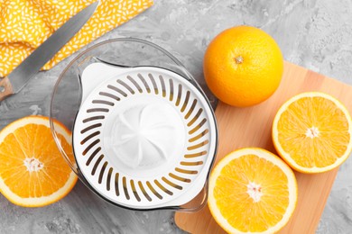 Photo of Plastic juicer, oranges and knife on grey table, top view