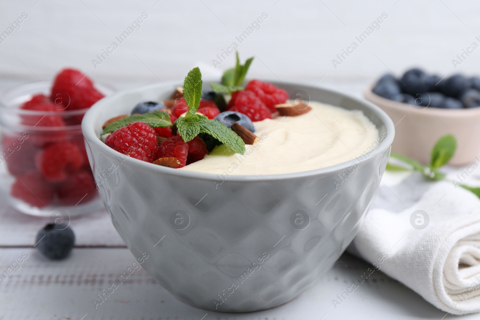 Photo of Tasty cooked semolina porridge with almonds, berries and mint on white wooden table, closeup