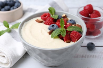 Photo of Tasty cooked semolina porridge with almonds, berries and mint on white wooden table, closeup