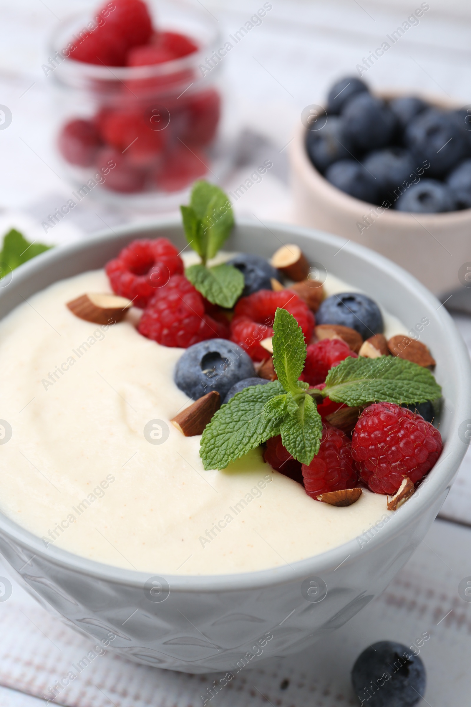 Photo of Tasty cooked semolina porridge with almonds, berries and mint on white wooden table, closeup