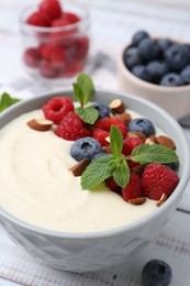 Tasty cooked semolina porridge with almonds, berries and mint on white wooden table, closeup