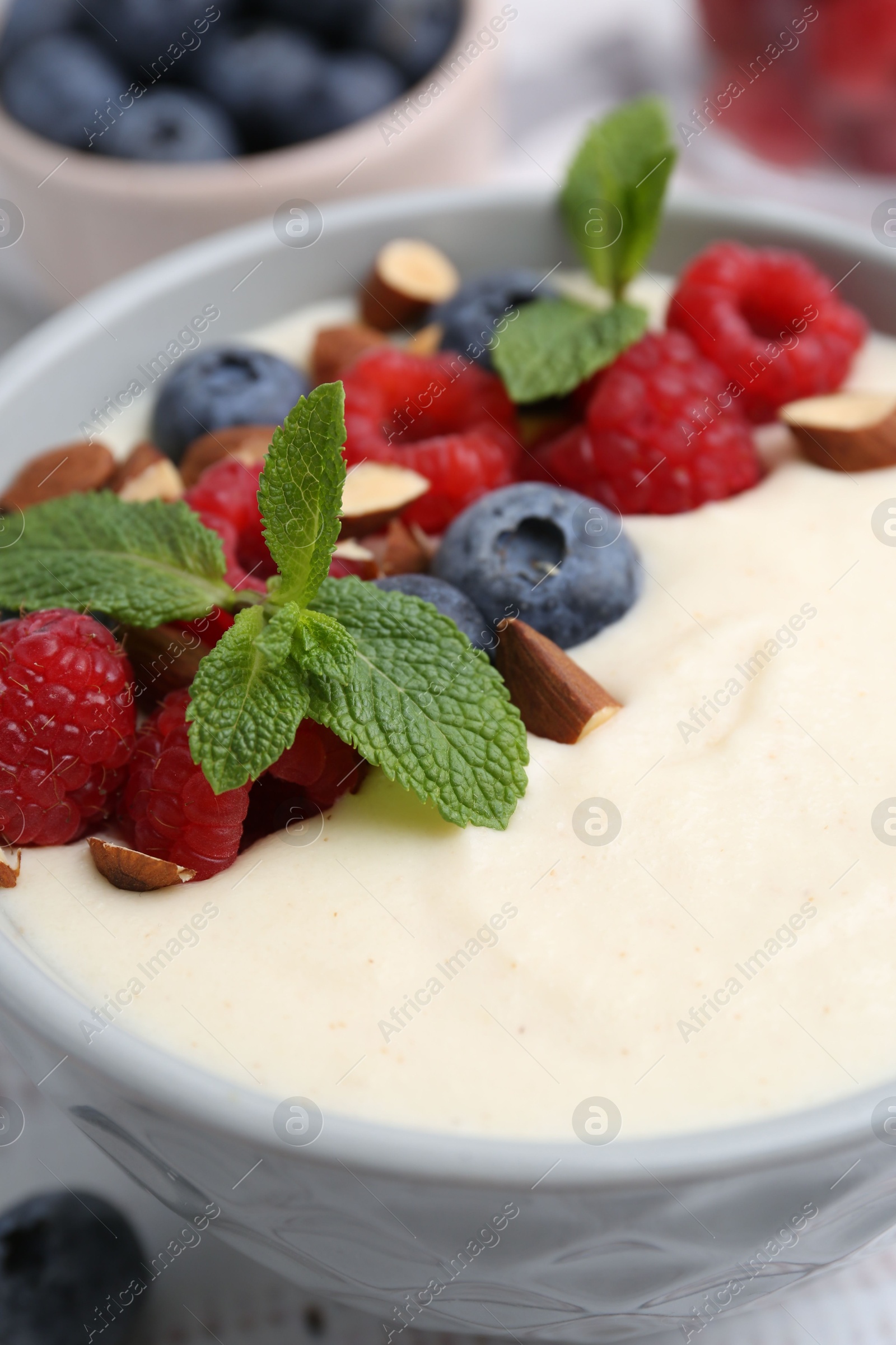 Photo of Tasty cooked semolina porridge with almonds, berries and mint on table, closeup