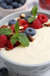 Photo of Tasty cooked semolina porridge with almonds, berries and mint on table, closeup