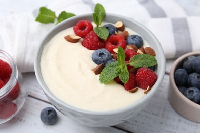 Tasty cooked semolina porridge with almonds, berries and mint on white wooden table, closeup