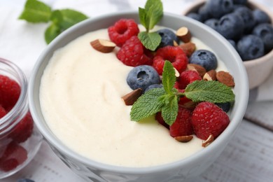 Photo of Tasty cooked semolina porridge with almonds, berries and mint on table, closeup