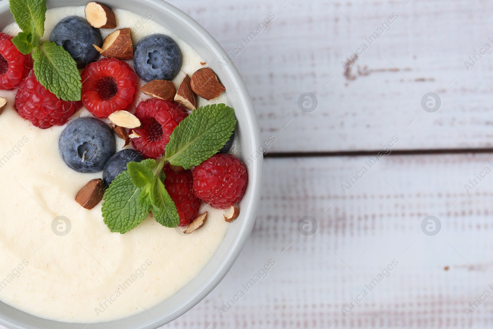 Photo of Tasty cooked semolina porridge with almonds, berries and mint on white wooden table, top view. Space for text