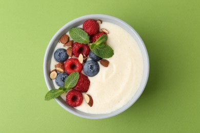 Tasty cooked semolina porridge with almonds, berries and mint on green background, top view