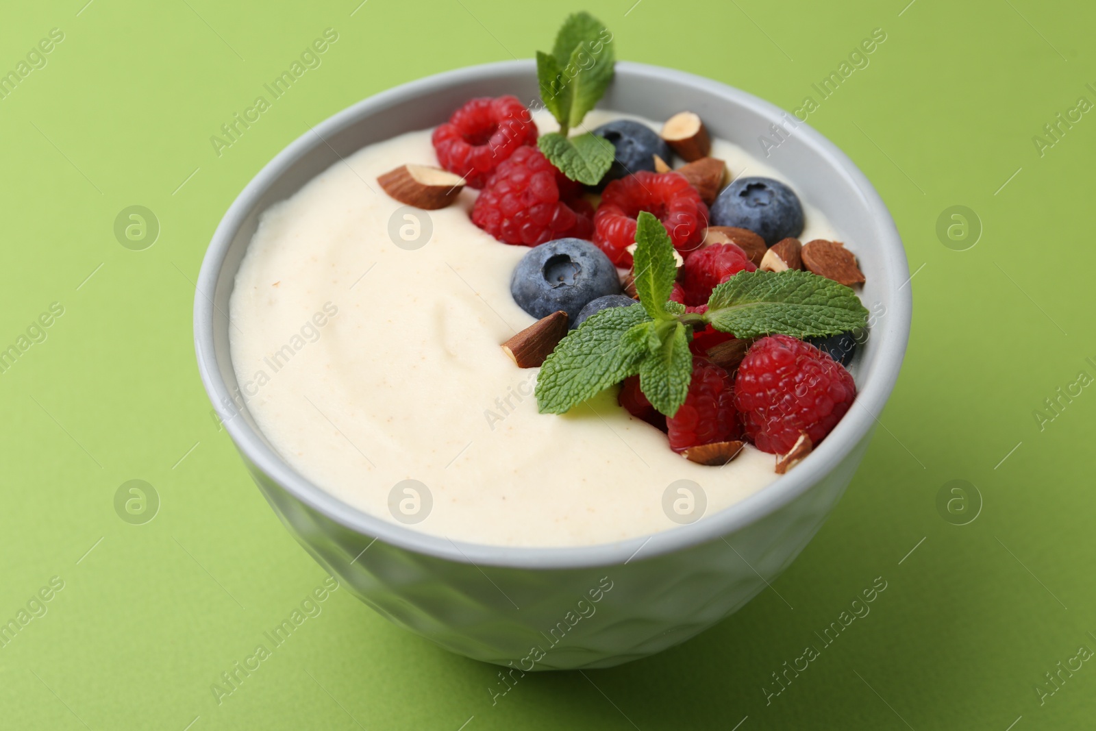 Photo of Tasty cooked semolina porridge with almonds, berries and mint on green background, closeup