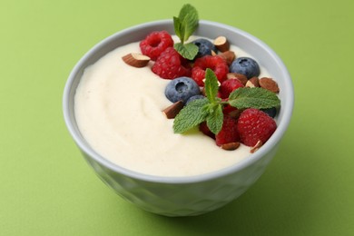 Tasty cooked semolina porridge with almonds, berries and mint on green background, closeup