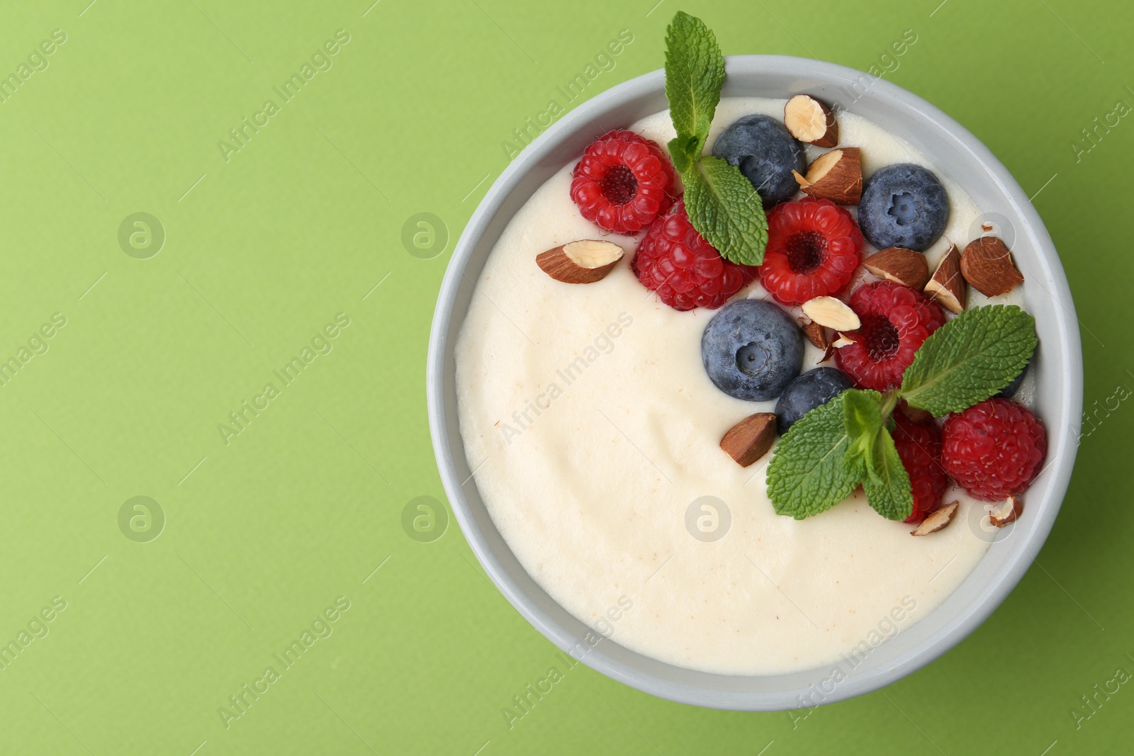 Photo of Tasty cooked semolina porridge with almonds, berries and mint on green background, top view. Space for text