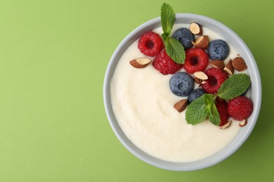 Photo of Tasty cooked semolina porridge with almonds, berries and mint on green background, top view. Space for text