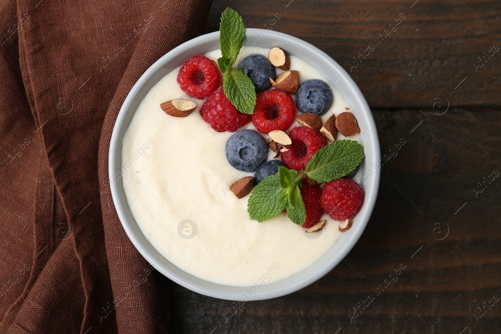 Photo of Tasty cooked semolina porridge with almonds, berries and mint on wooden table, top view