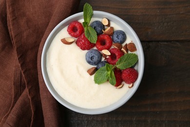 Photo of Tasty cooked semolina porridge with almonds, berries and mint on wooden table, top view