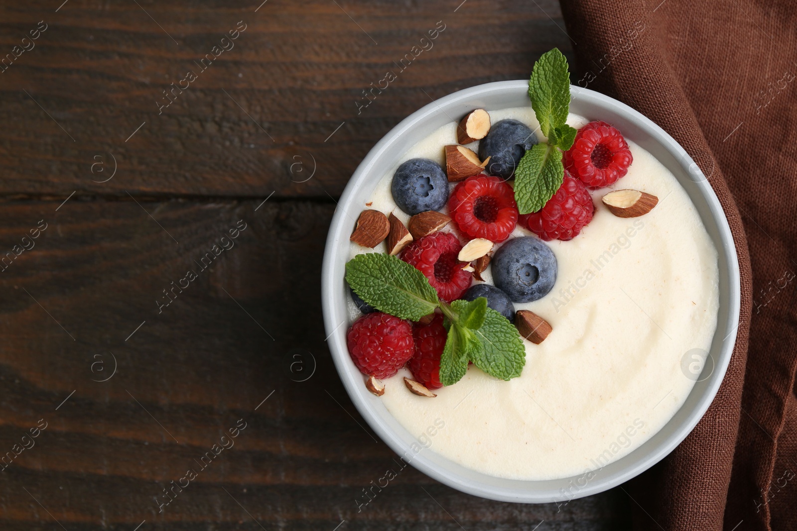 Photo of Tasty cooked semolina porridge with almonds, berries and mint on wooden table, top view. Space for text