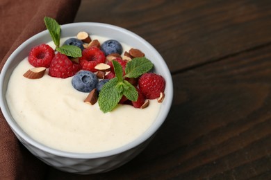 Tasty cooked semolina porridge with almonds, berries and mint on wooden table, closeup. Space for text