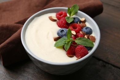 Tasty cooked semolina porridge with almonds, berries and mint on wooden table, closeup