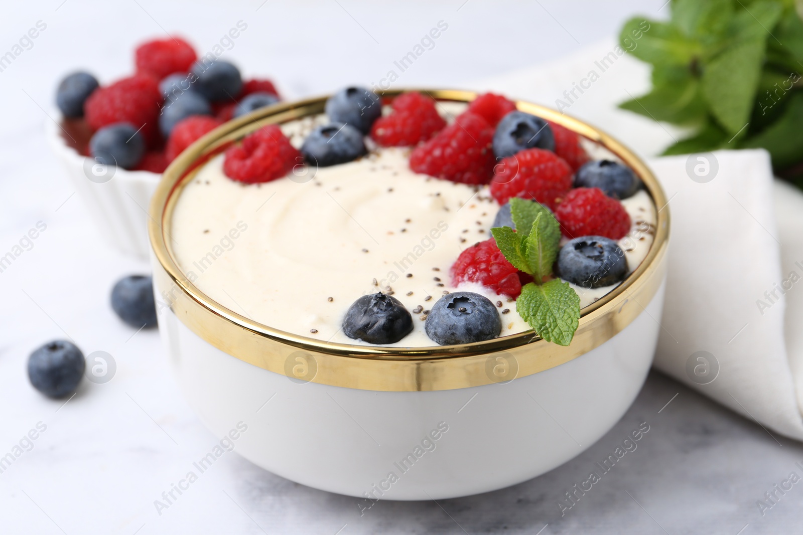 Photo of Tasty cooked semolina porridge with berries and mint on white marble table, closeup