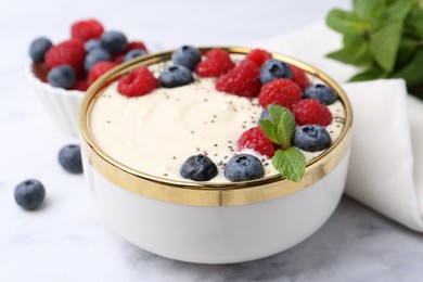 Tasty cooked semolina porridge with berries and mint on white marble table, closeup