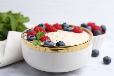 Tasty cooked semolina porridge with berries and mint on white marble table, closeup