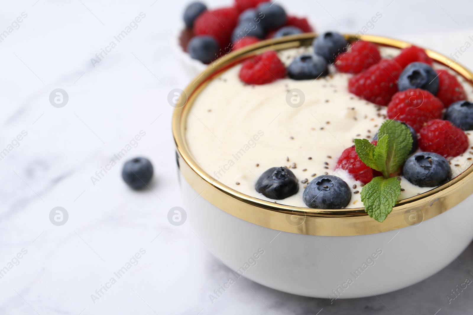 Photo of Tasty cooked semolina porridge with berries and mint on white marble table, closeup. Space for text