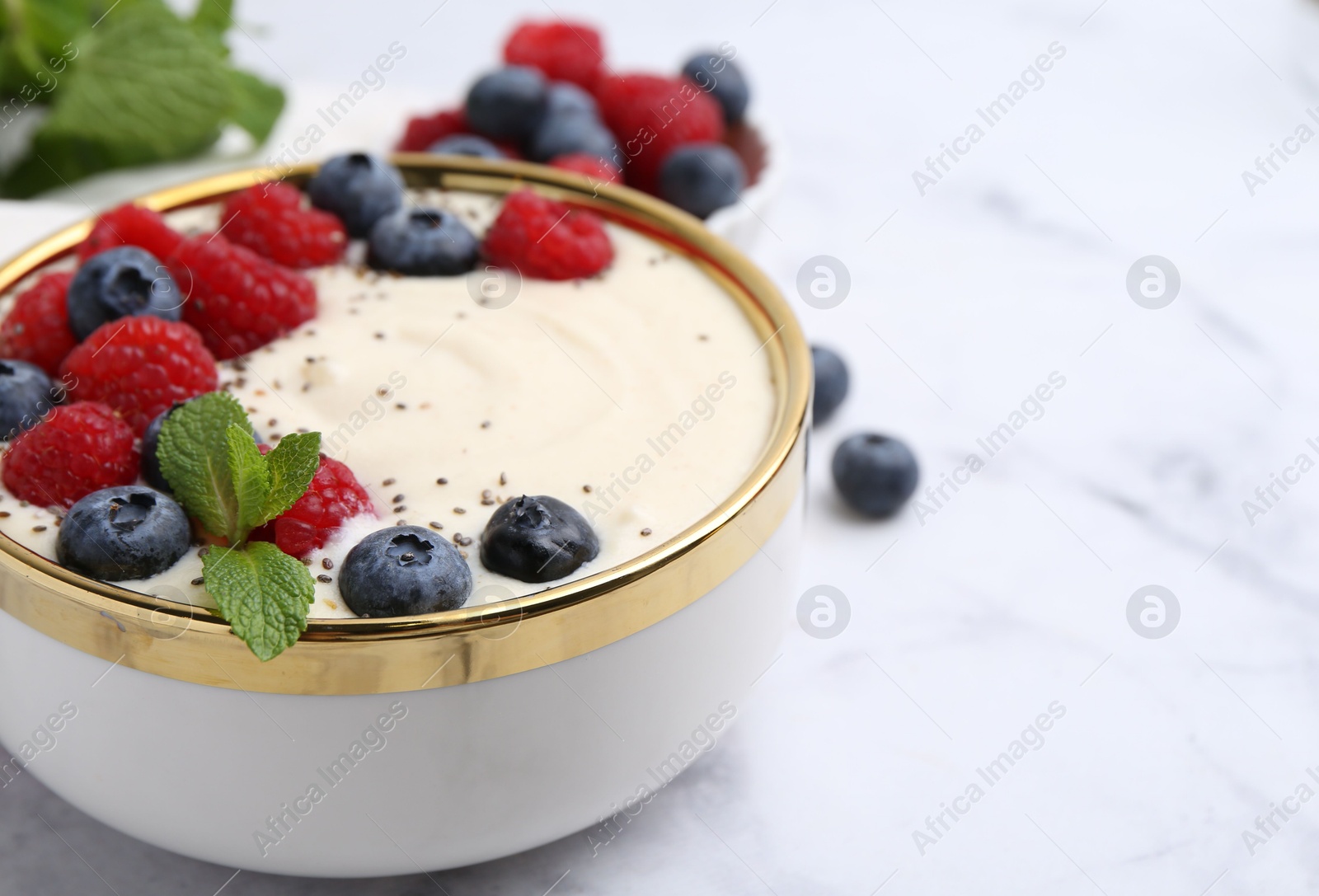 Photo of Tasty cooked semolina porridge with berries and mint on white marble table, closeup. Space for text