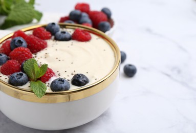 Tasty cooked semolina porridge with berries and mint on white marble table, closeup. Space for text