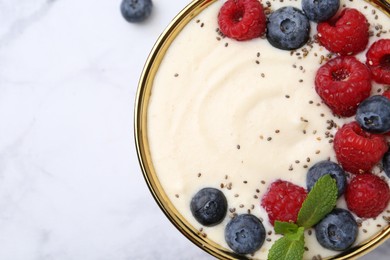 Tasty cooked semolina porridge with berries and mint on white table, top view. Space for text