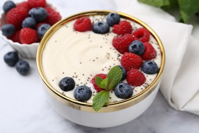 Tasty cooked semolina porridge with berries and mint on white marble table, closeup