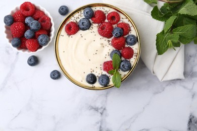 Tasty cooked semolina porridge with berries and mint on white marble table, top view