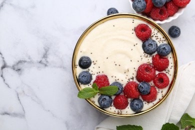 Photo of Tasty cooked semolina porridge with berries and mint on white marble table, top view. Space for text