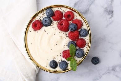 Tasty cooked semolina porridge with berries and mint on white marble table, top view