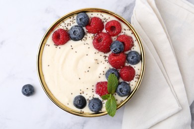 Tasty cooked semolina porridge with berries and mint on white marble table, top view