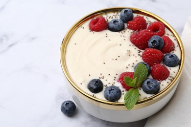 Photo of Tasty cooked semolina porridge with berries and mint on white marble table, closeup