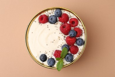 Tasty cooked semolina porridge with berries and mint on pale brown background, top view