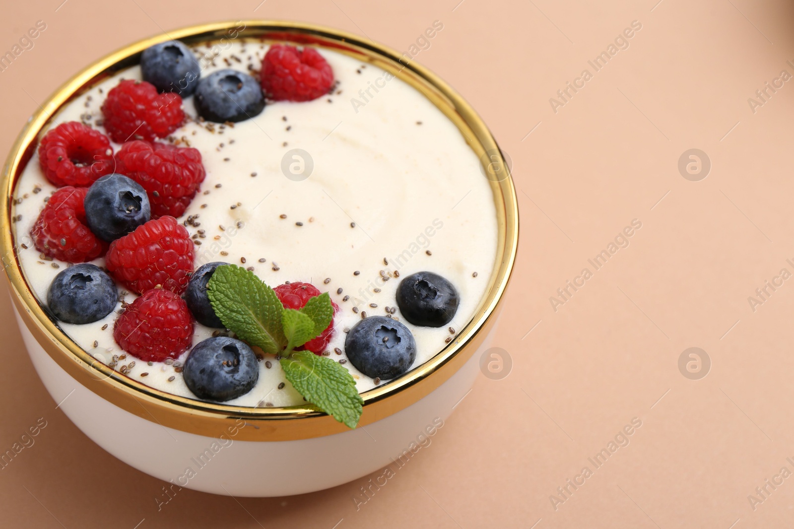 Photo of Tasty cooked semolina porridge with berries and mint on pale brown background, closeup. Space for text