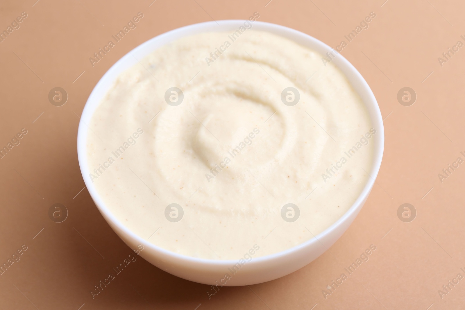 Photo of Tasty cooked semolina porridge in bowl on pale brown background, closeup