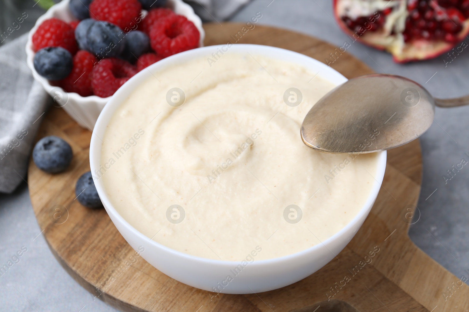 Photo of Tasty cooked semolina porridge in bowl and berries on grey table, closeup