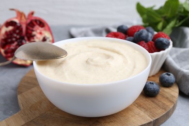 Photo of Tasty cooked semolina porridge in bowl and berries on grey table, closeup