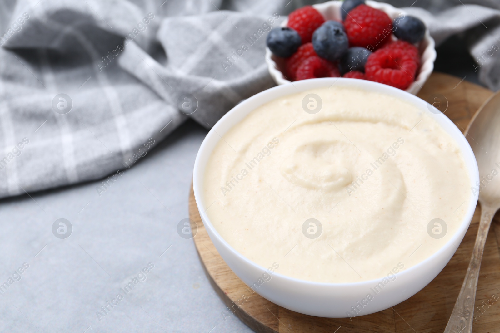 Photo of Tasty cooked semolina porridge in bowl and berries on grey table, closeup. Space for text