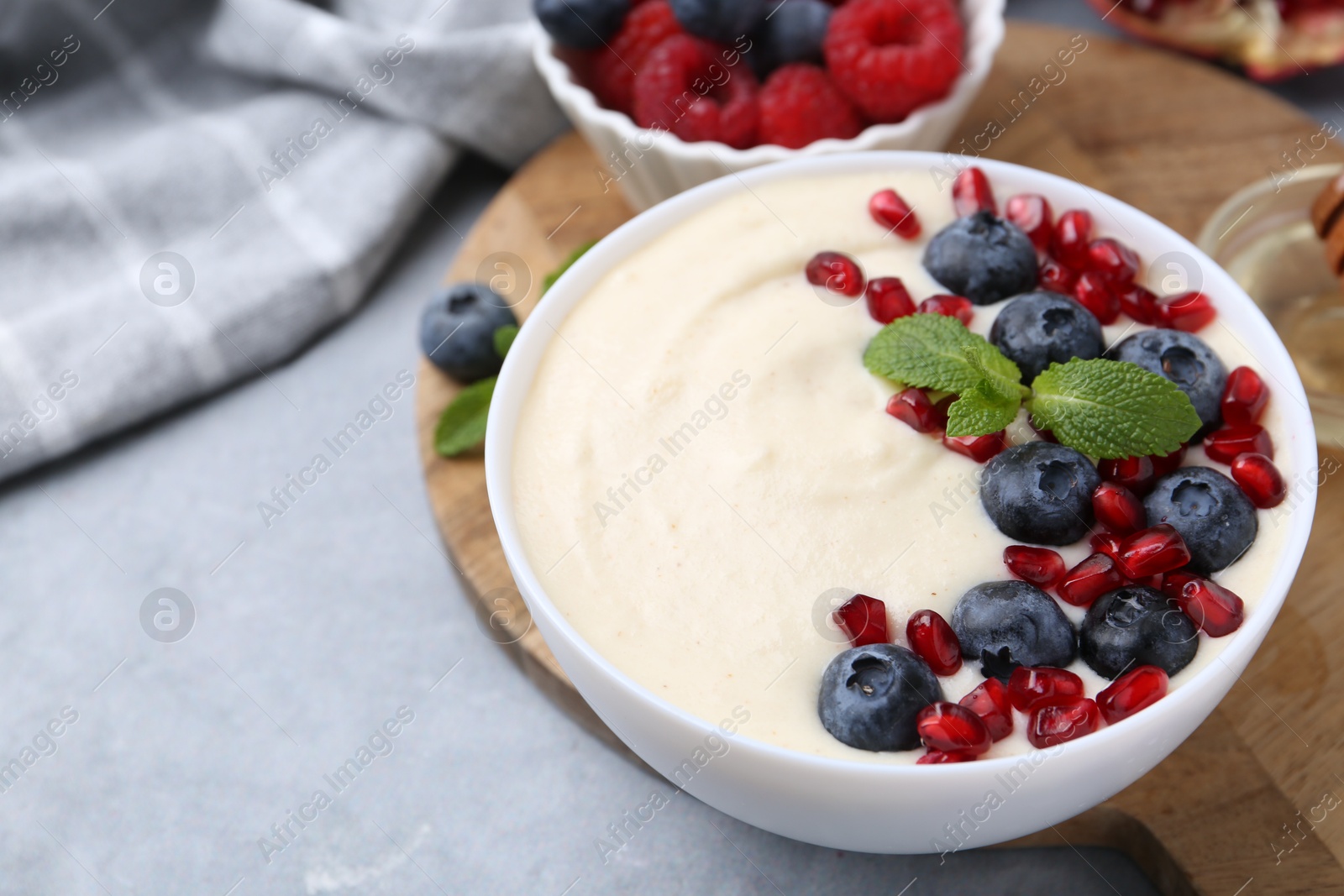 Photo of Tasty cooked semolina porridge with blueberries, pomegranate and mint on grey table, closeup. Space for text