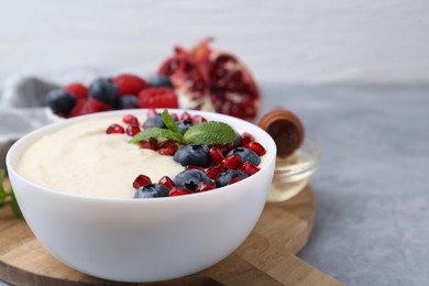 Tasty cooked semolina porridge with blueberries, pomegranate and mint on grey table, closeup. Space for text