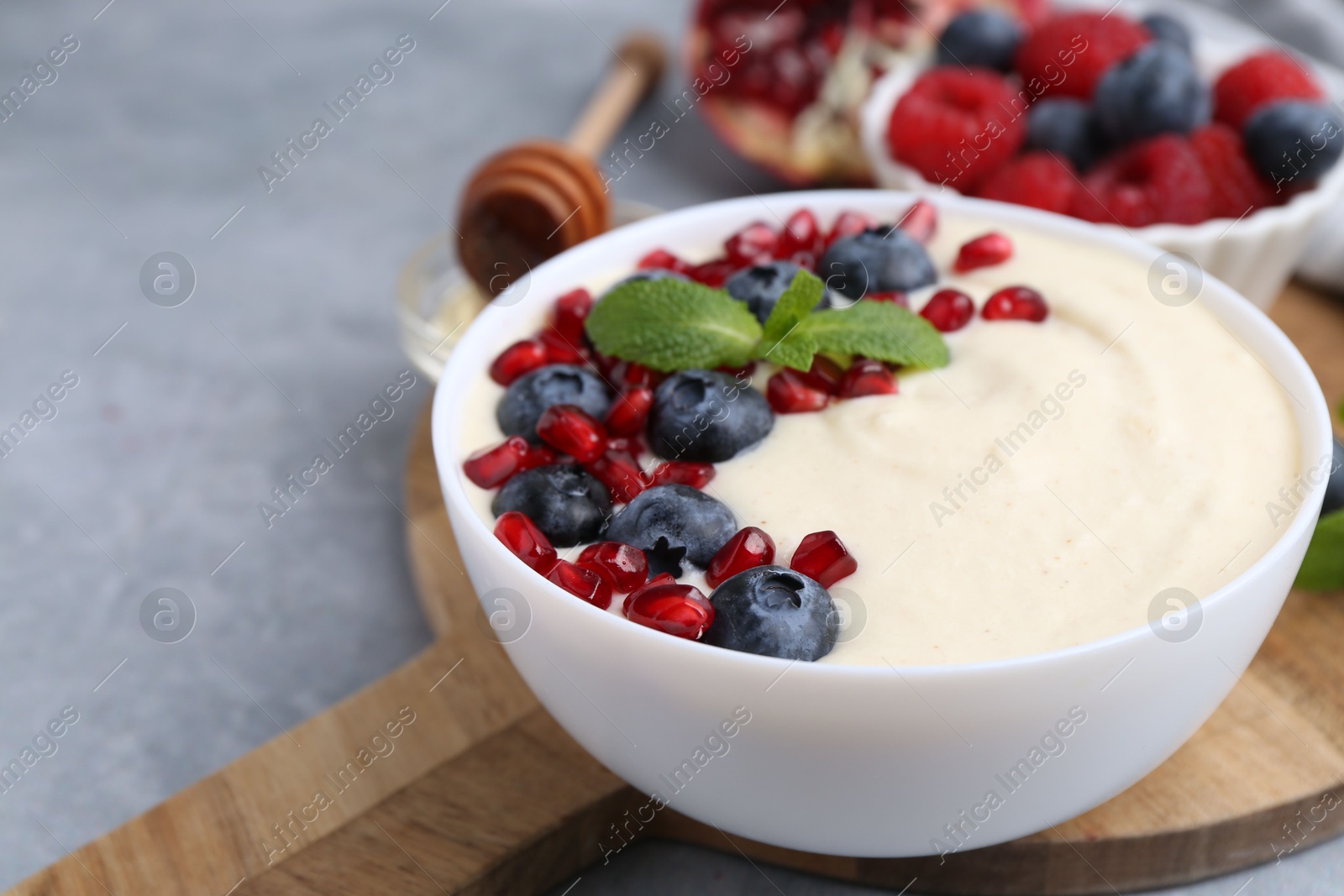 Photo of Tasty cooked semolina porridge with blueberries, pomegranate and mint on grey table, closeup