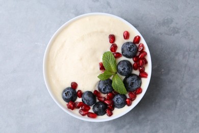 Tasty cooked semolina porridge with blueberries, pomegranate and mint on grey table, top view