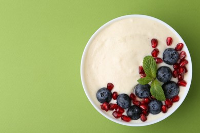 Tasty cooked semolina porridge with blueberries, pomegranate and mint on green background, top view. Space for text