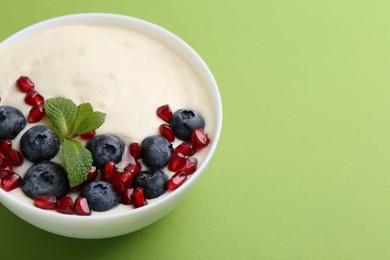 Photo of Tasty cooked semolina porridge with blueberries, pomegranate and mint on green background, closeup. Space for text