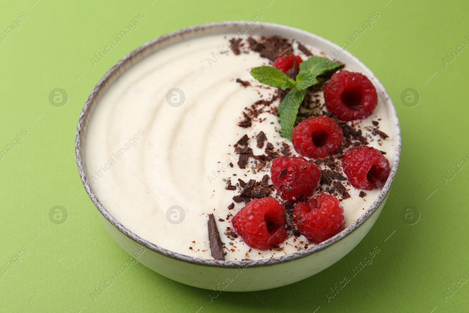 Photo of Tasty cooked semolina porridge with raspberries, chocolate and mint on green background, closeup