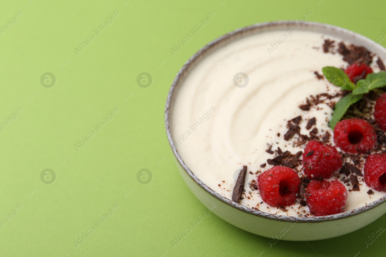 Photo of Tasty cooked semolina porridge with raspberries, chocolate and mint on green background, closeup. Space for text