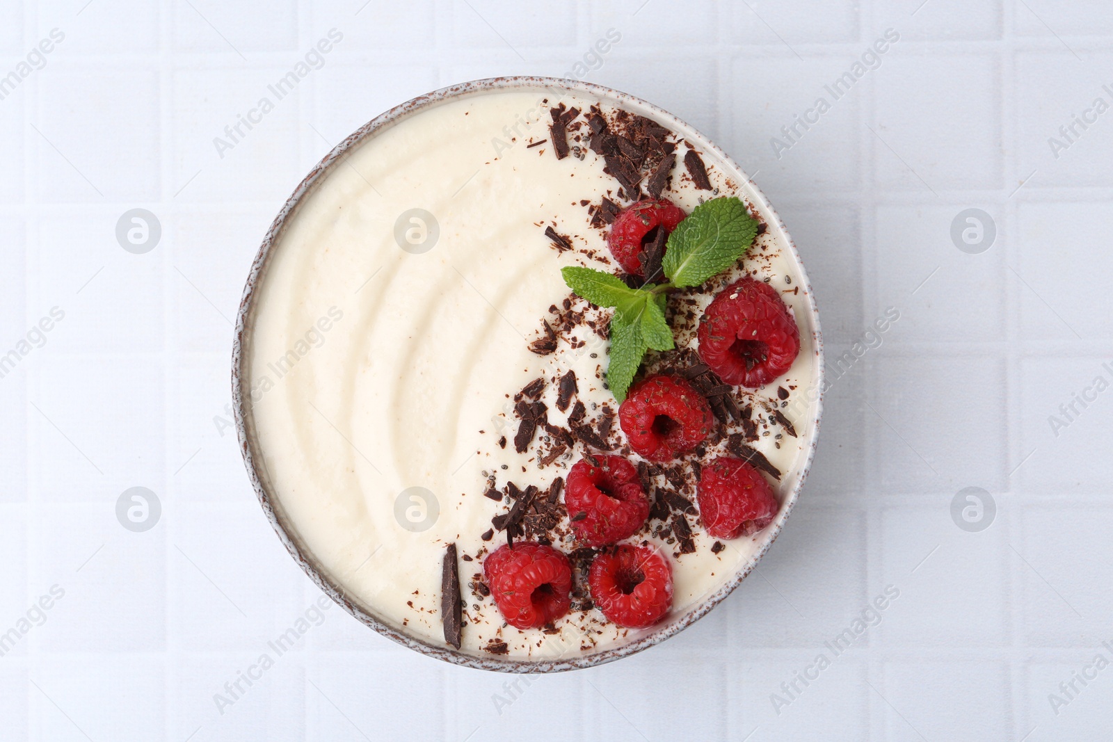 Photo of Tasty cooked semolina porridge with raspberries, chocolate and mint on white tiled table, top view