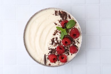 Tasty cooked semolina porridge with raspberries, chocolate and mint on white tiled table, top view