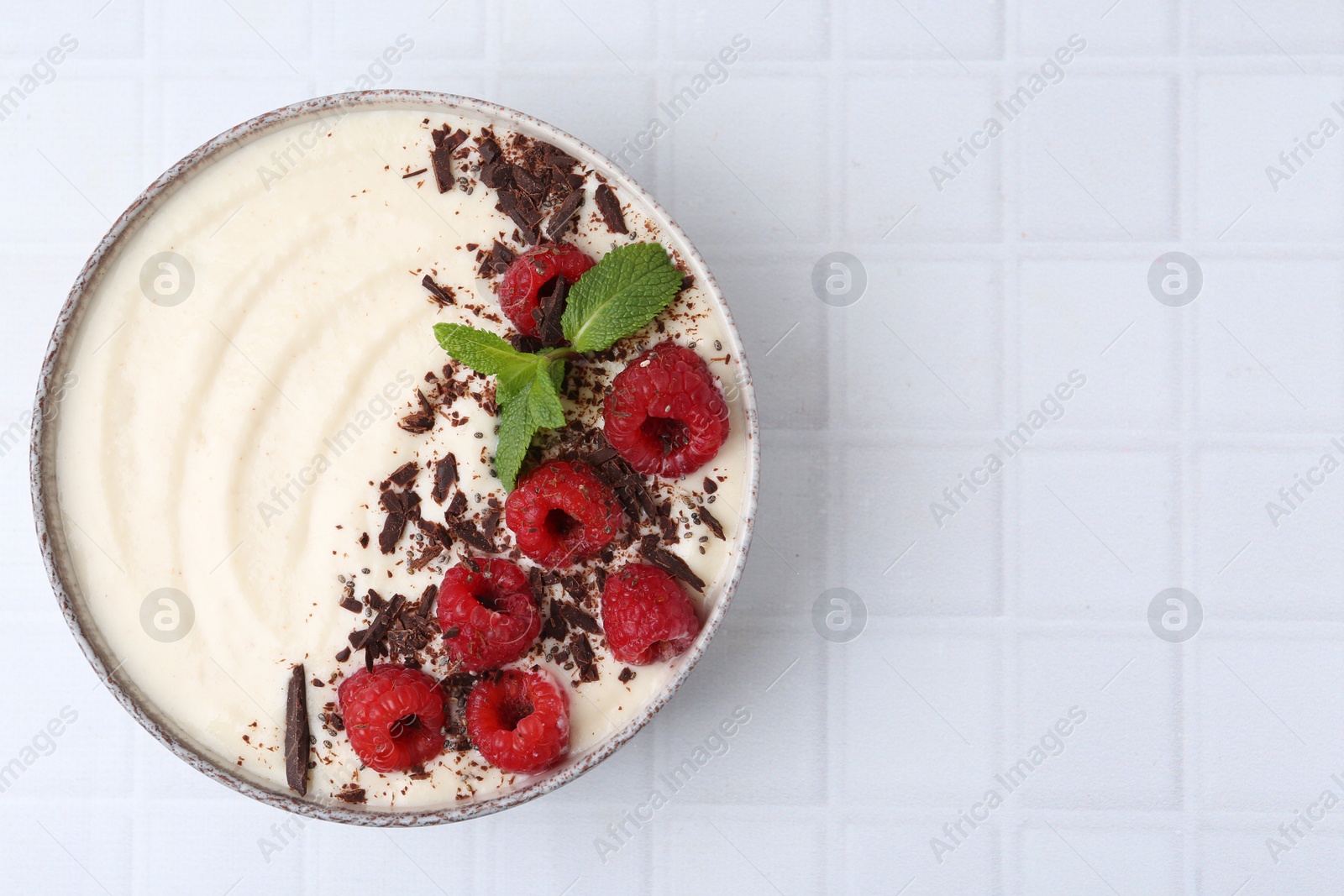 Photo of Tasty cooked semolina porridge with raspberries, chocolate and mint on white tiled table, top view. Space for text